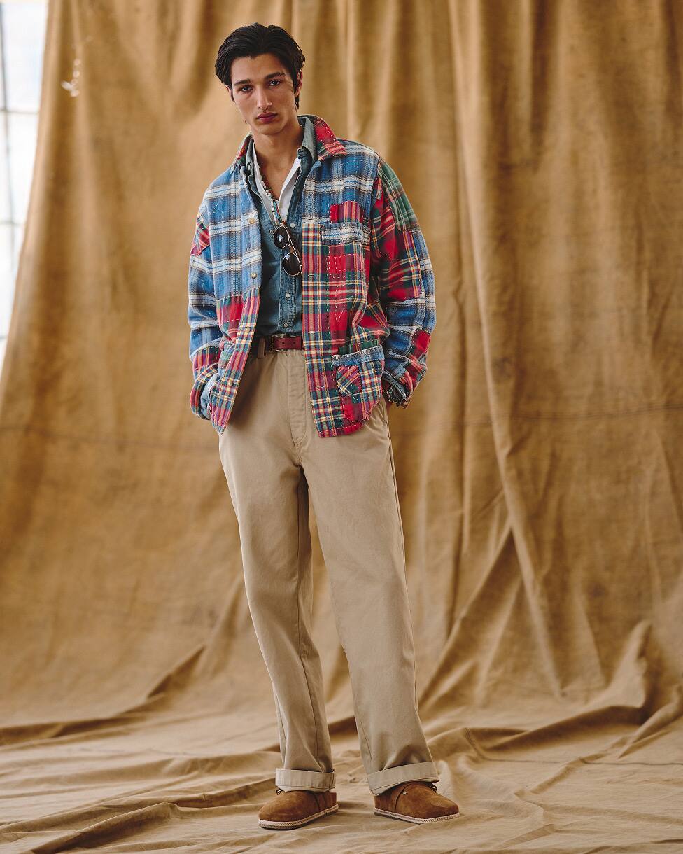 Man met een flanellen overhemd over een denim overhemd, beige broek en loafers.