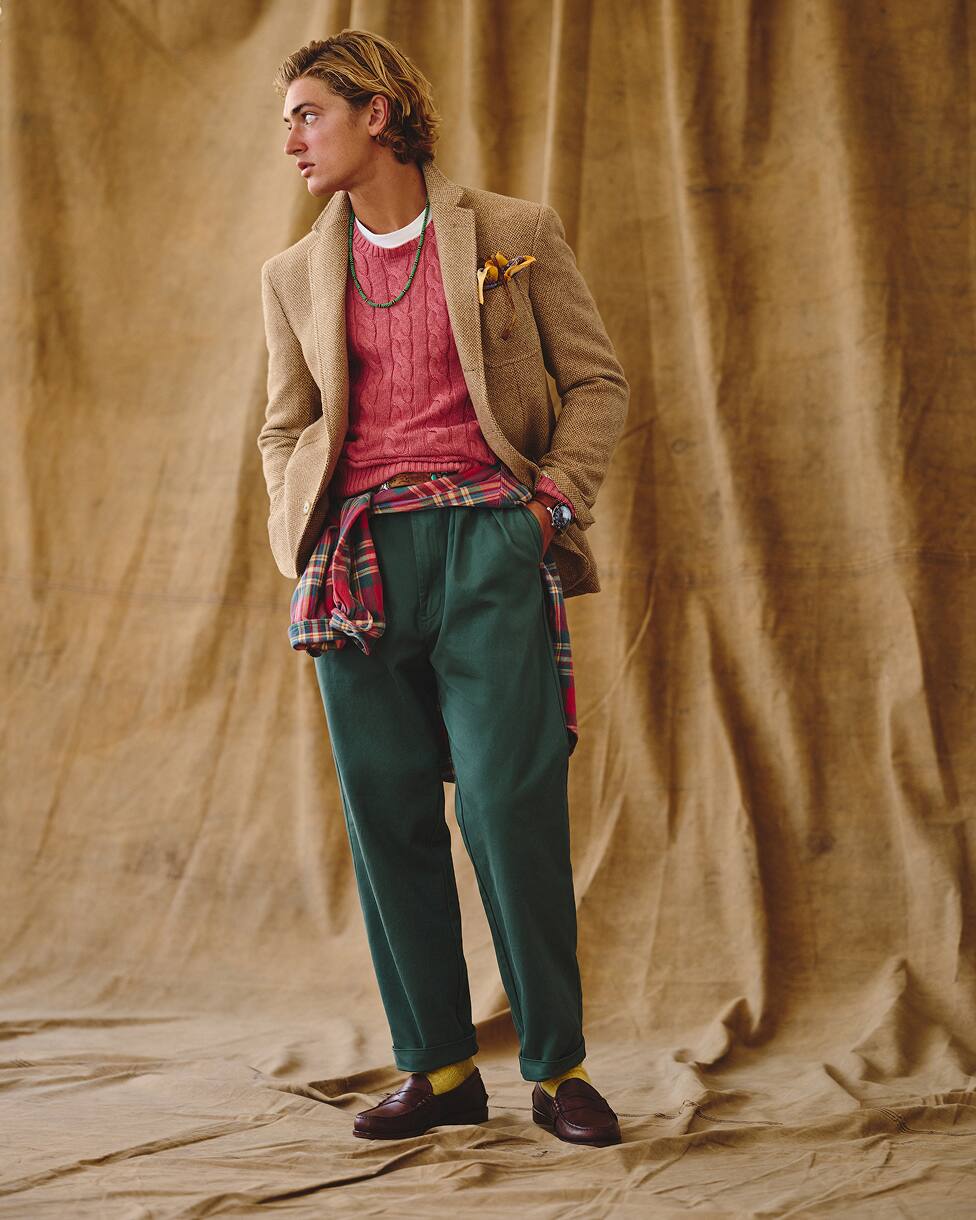 Man in een rode trui, beige blazer, spijkerbroek en loafers.